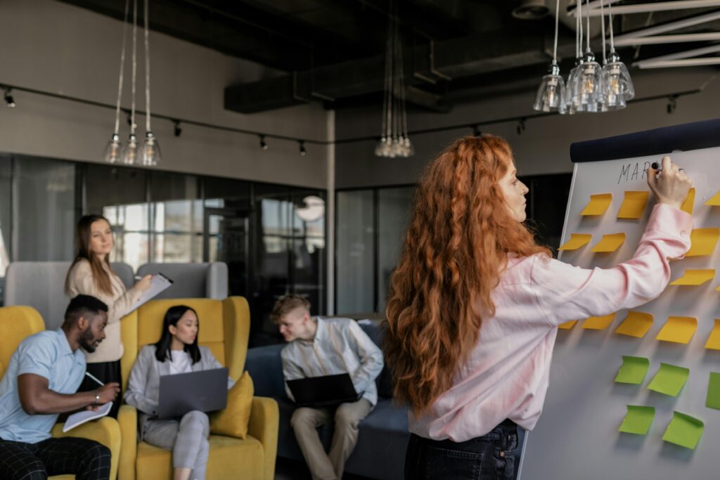 A marketing team gathered around a whiteboard mapping campaign steps, goals, and audience messaging.